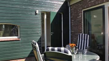 Un'area patio con tavolo e sedie, una porta scorrevole in vetro e una parete esterna verde.