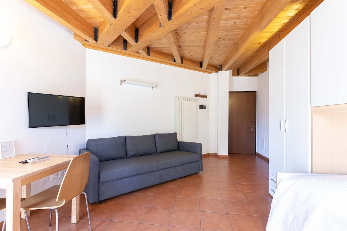 Une chambre moderne avec un plafond en bois, un canapé gris, un bureau en bois et un lit.