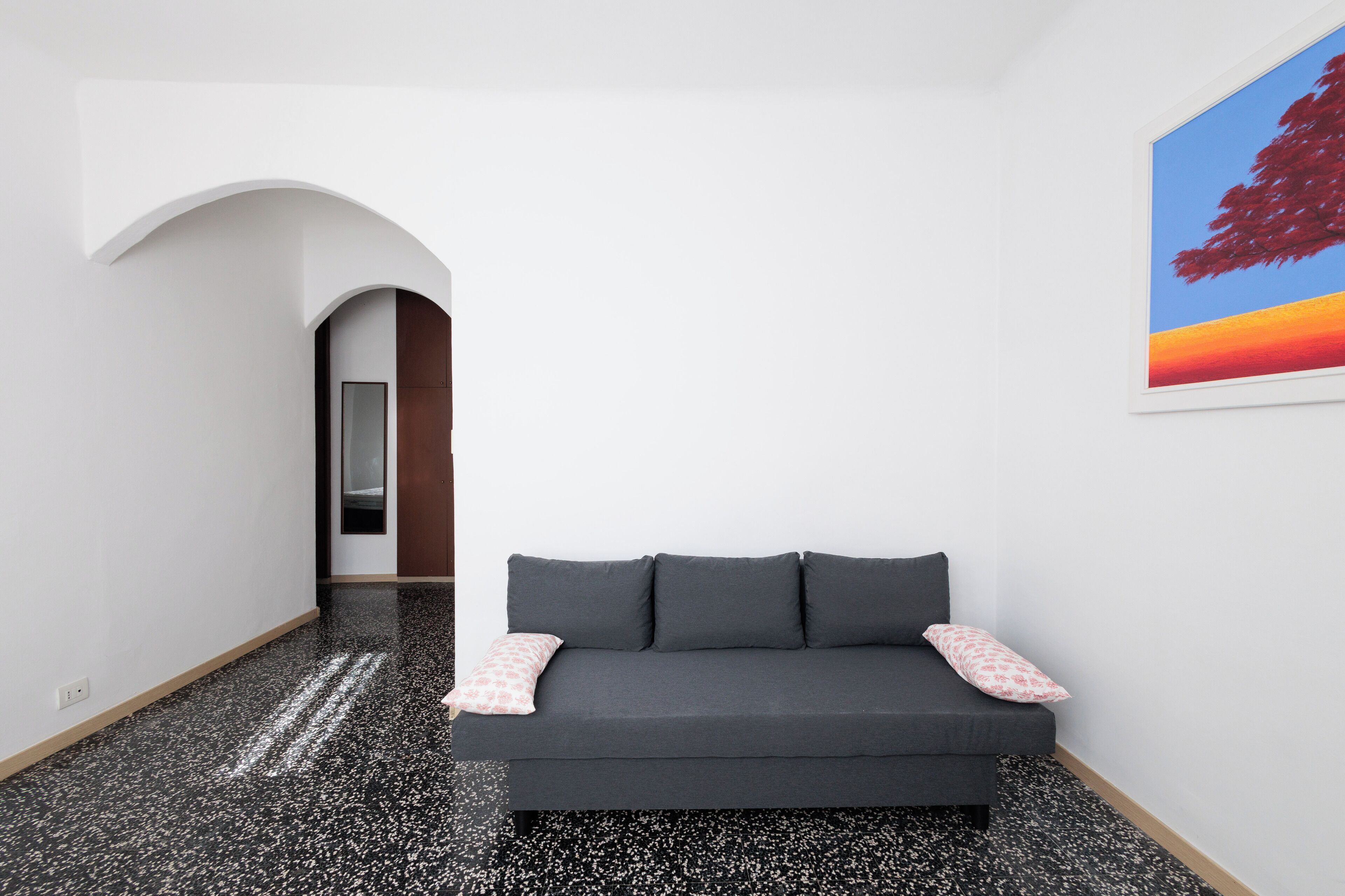 Un interior moderno con un sofá gris oscuro, un cojín estampado en rosa y un cuadro grande de un árbol al atardecer.