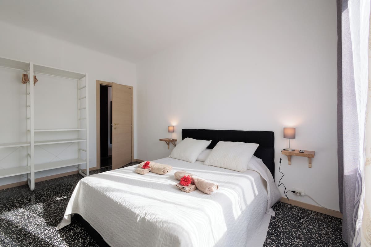 Un lit bien fait, avec du linge de lit blanc et des serviettes décoratives, une tête de lit en bois, des lampes de chevet et une armoire avec un miroir.