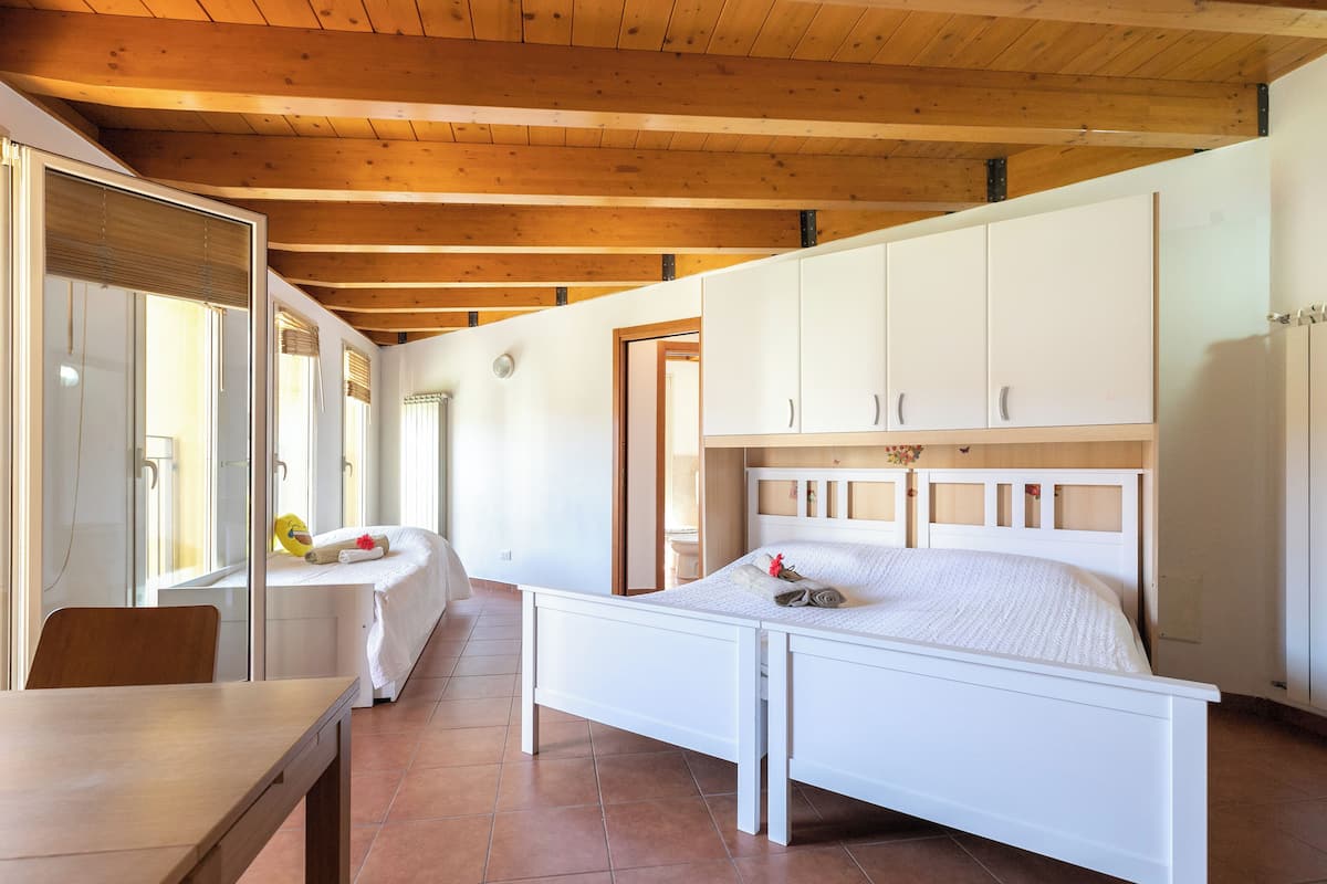 Une chambre avec un plafond en bois, un lit blanc et un bureau avec une chaise.