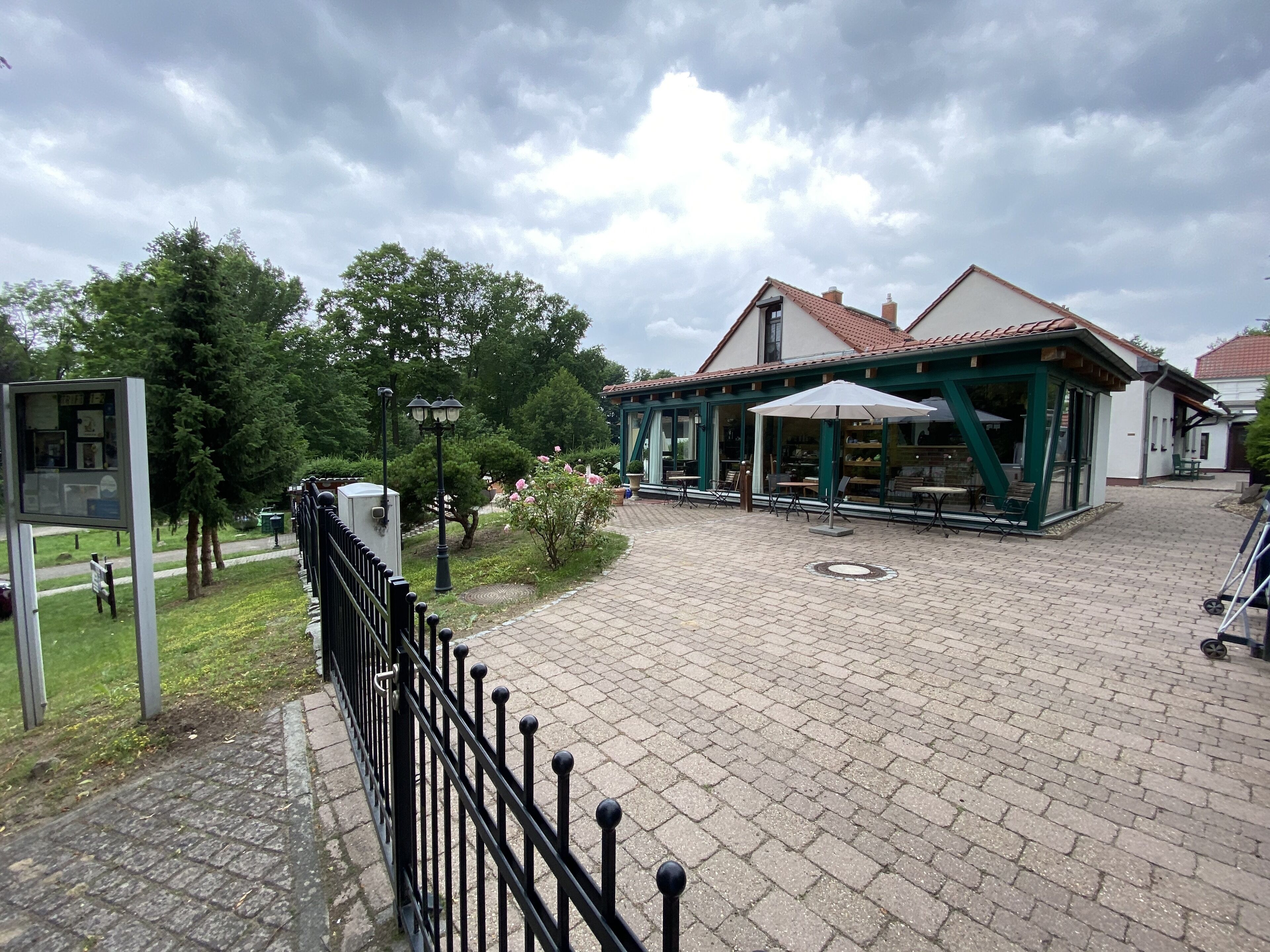 A covered outdoor seating area with tables and chairs, a paved walkway, and a fence.