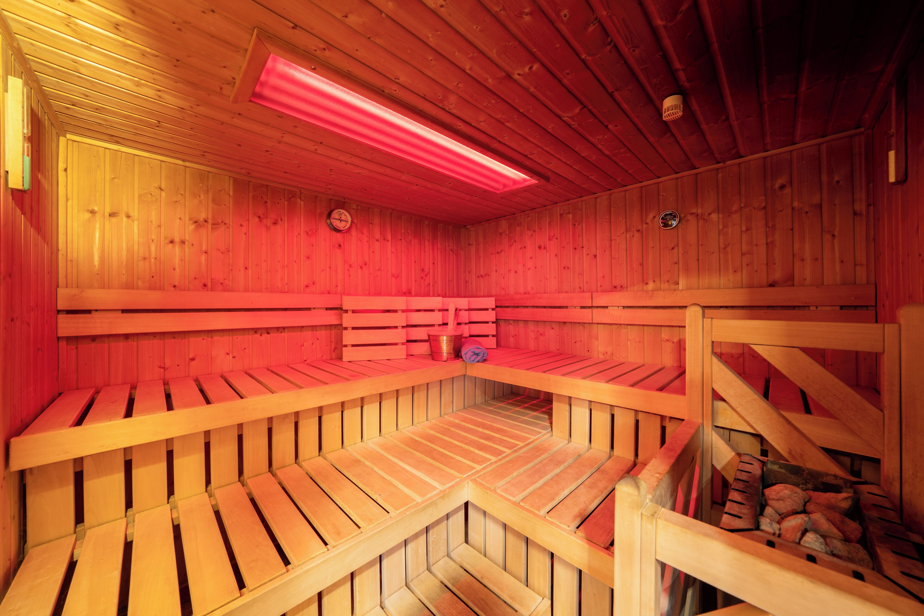 Een sauna met houten banken en vloer, en een rood verlicht plafond.