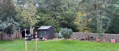 A backyard with a small wooden shed, a stone wall, and a variety of trees and shrubs.