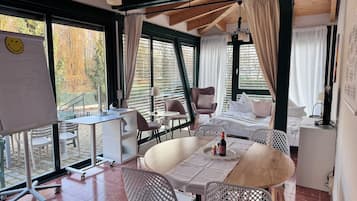 A modern hotel room with a large dining table, comfortable seating, a whiteboard with a smiley face, and large windows offering a view of the outdoors.