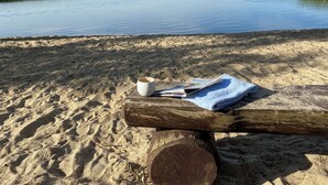 Una playa arenosa con un tronco de madera, una taza blanca y un periódico.