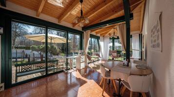 Una habitación amplia con ventanas grandes, techo de madera y un comedor con mesa y sillas.