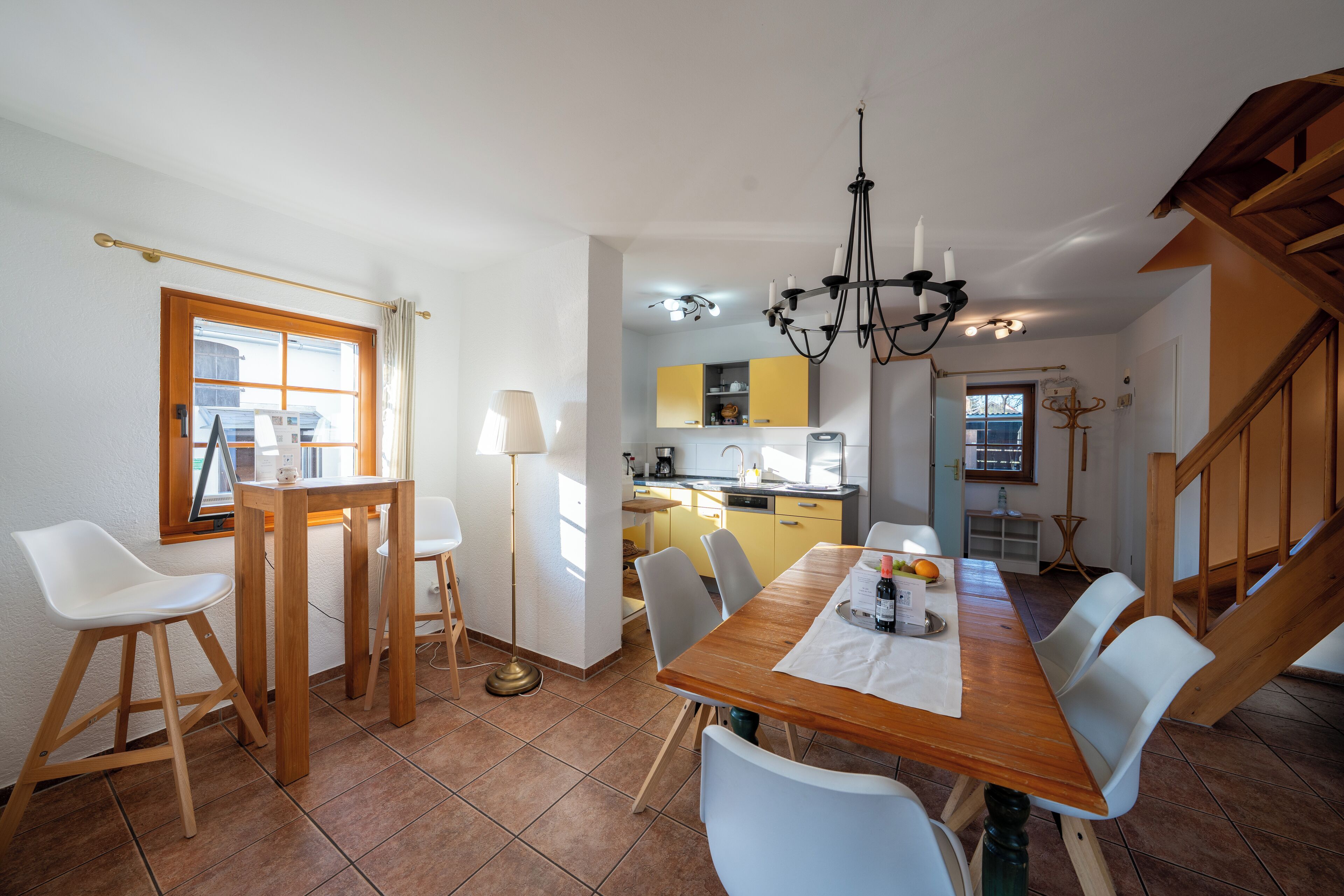 Un comedor con una mesa de madera, sillas blancas y una l ámpara de araña.