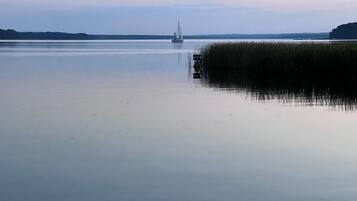 Une étendue d’eau calme, avec un voilier à l’horizon, bordée de rives verdoyantes.