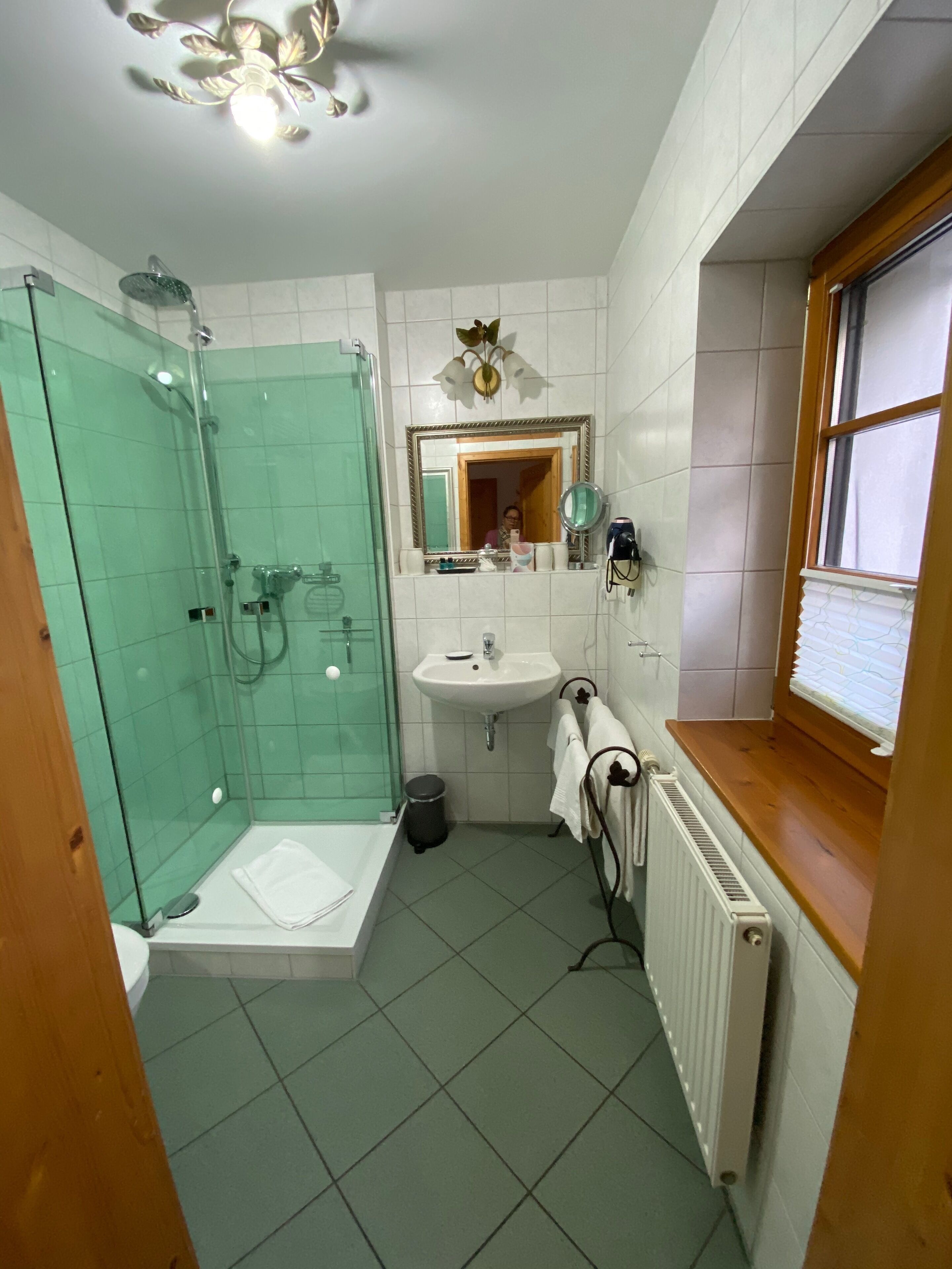 A bathroom with a glass-enclosed shower, a sink, a mirror, and a window.