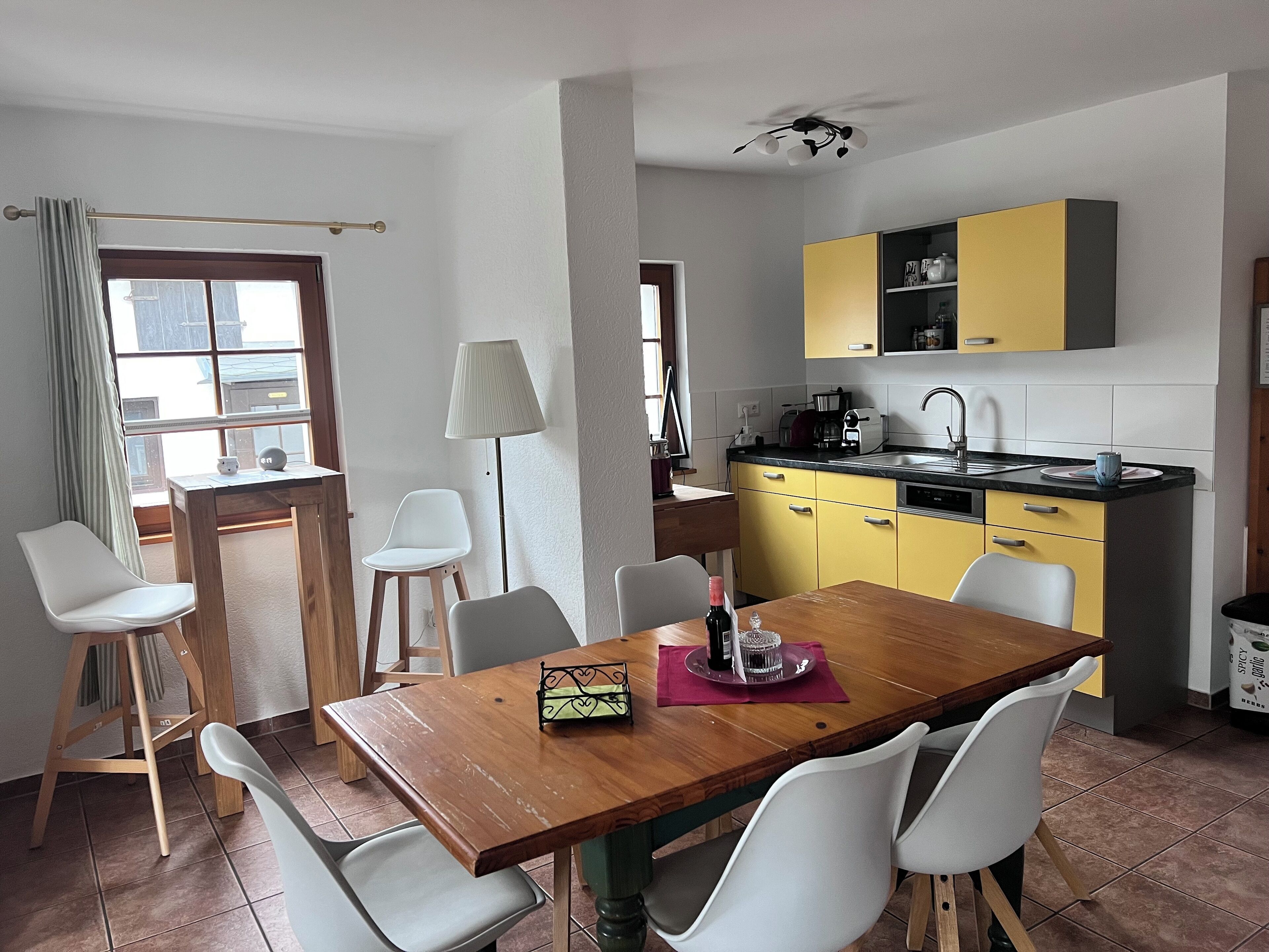 A compact kitchen with yellow cabinets, a wooden dining table, and white chairs.