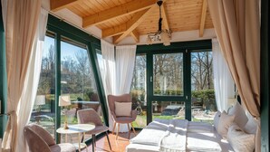 Una habitación acogedora con cama, dos sillas, una mesita y ventanas amplias que ofrecen vistas al exterior.