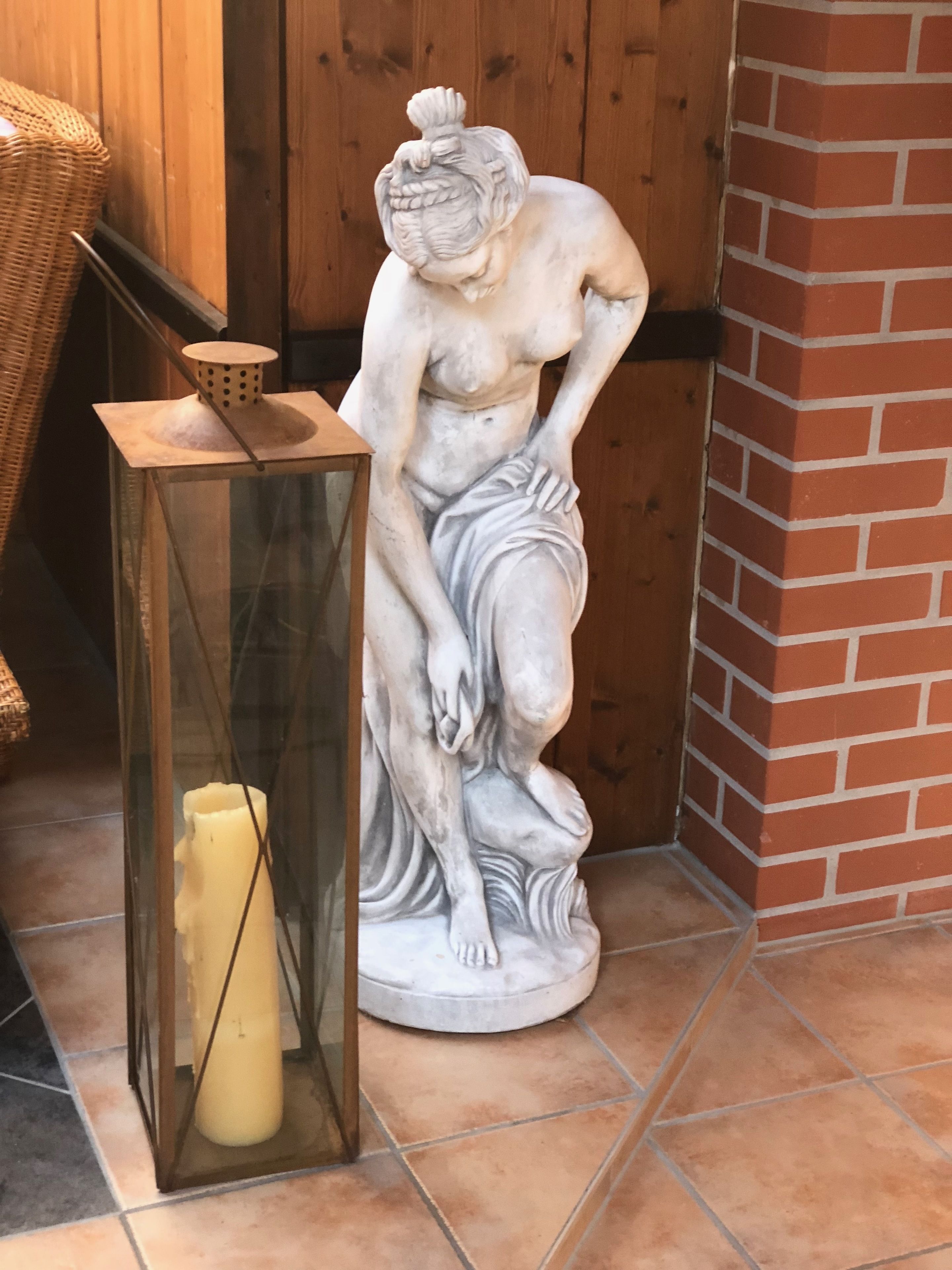 Eine Statue einer sitzenden Frau mit einem Korb auf einem Tisch neben einer Kerze in einer Glaskuppel.