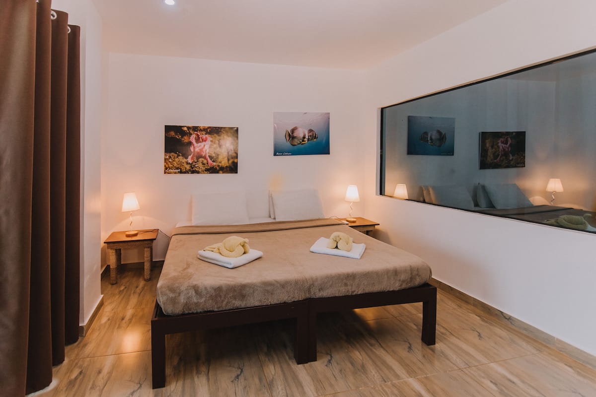 Une chambre d’hôtel avec un lit, deux tables de chevet, un grand miroir et des œuvres d’art accrochées aux murs.