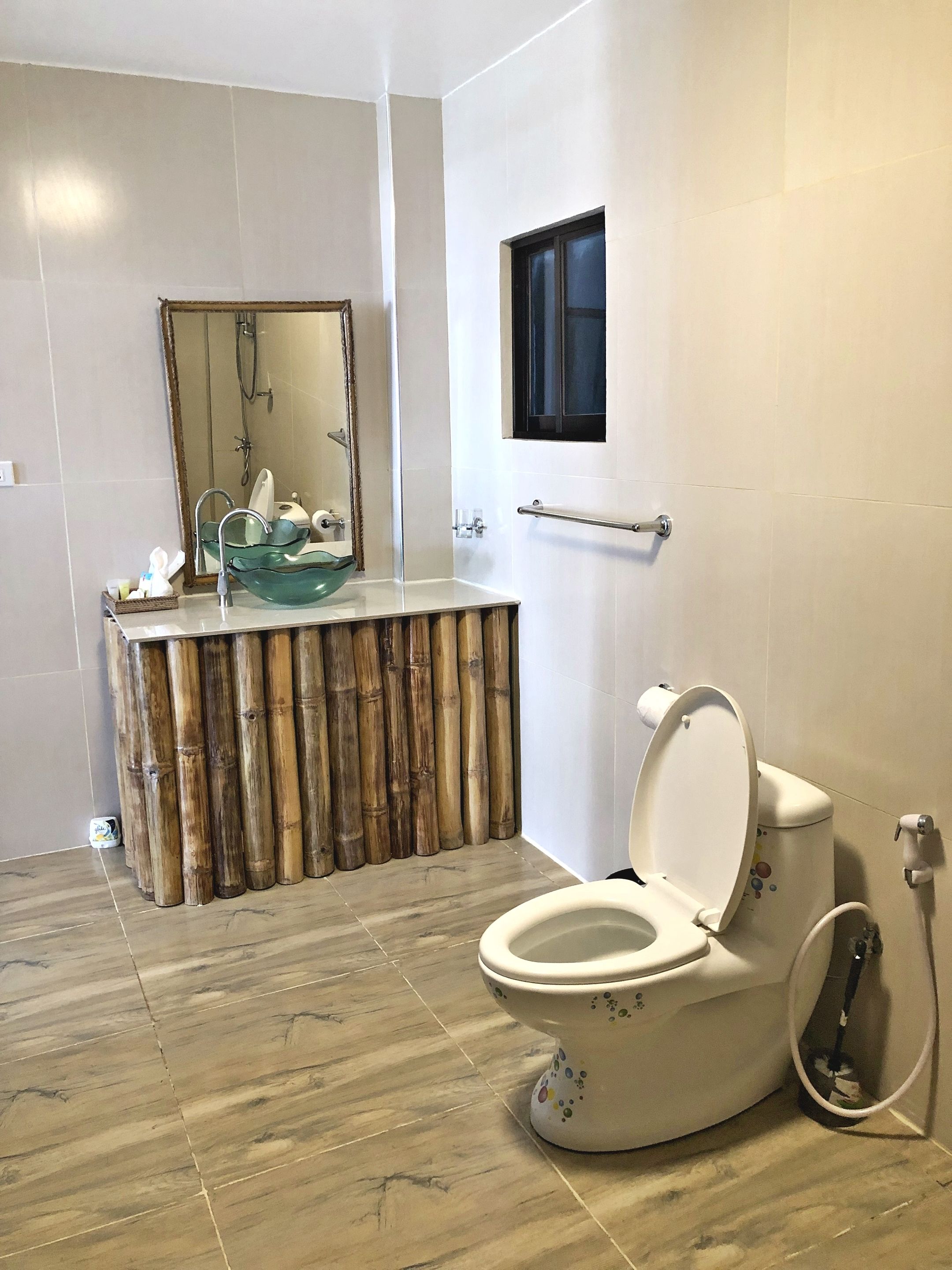 Un baño con inodoro, tocador de estilo bambú, lavamanos de cristal y ducha.