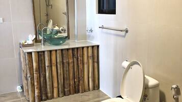 Un baño con inodoro, tocador de estilo bambú, lavamanos de cristal y ducha.