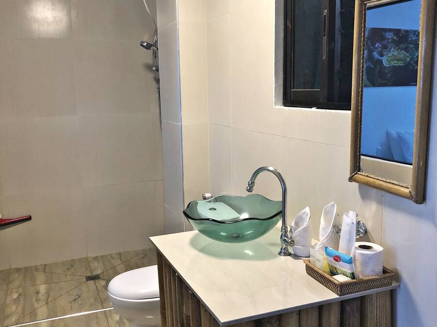 A bathroom with a glass bowl sink, a toilet, a shower, and a framed picture on the wall.