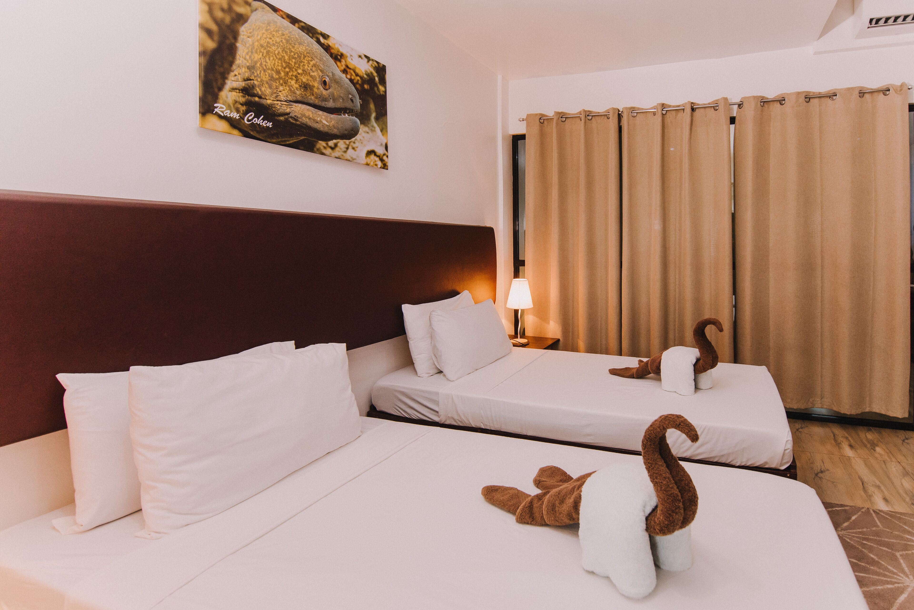 Een hotelkamer met twee bedden, een hoofdbord, een lamp, een gordijn en een aan de muur hangend schilderij.
