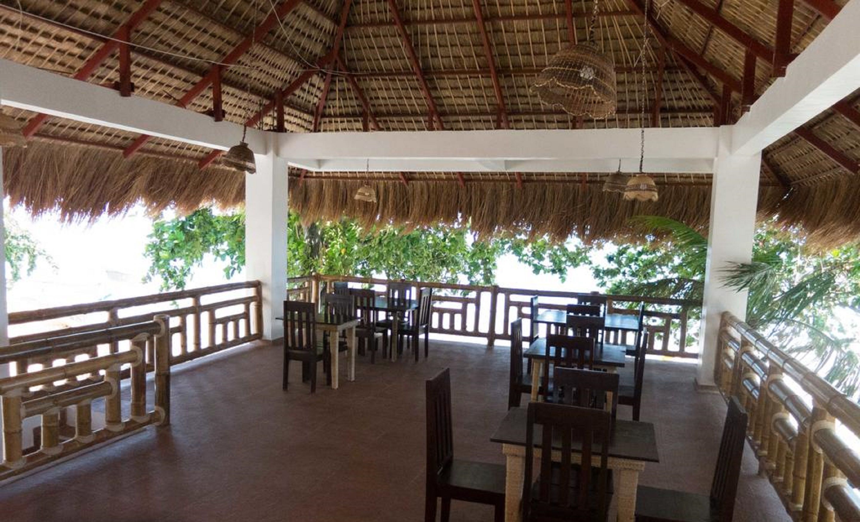 An open-air restaurant with thatched roofs, wooden furniture, and a view of lush greenery.