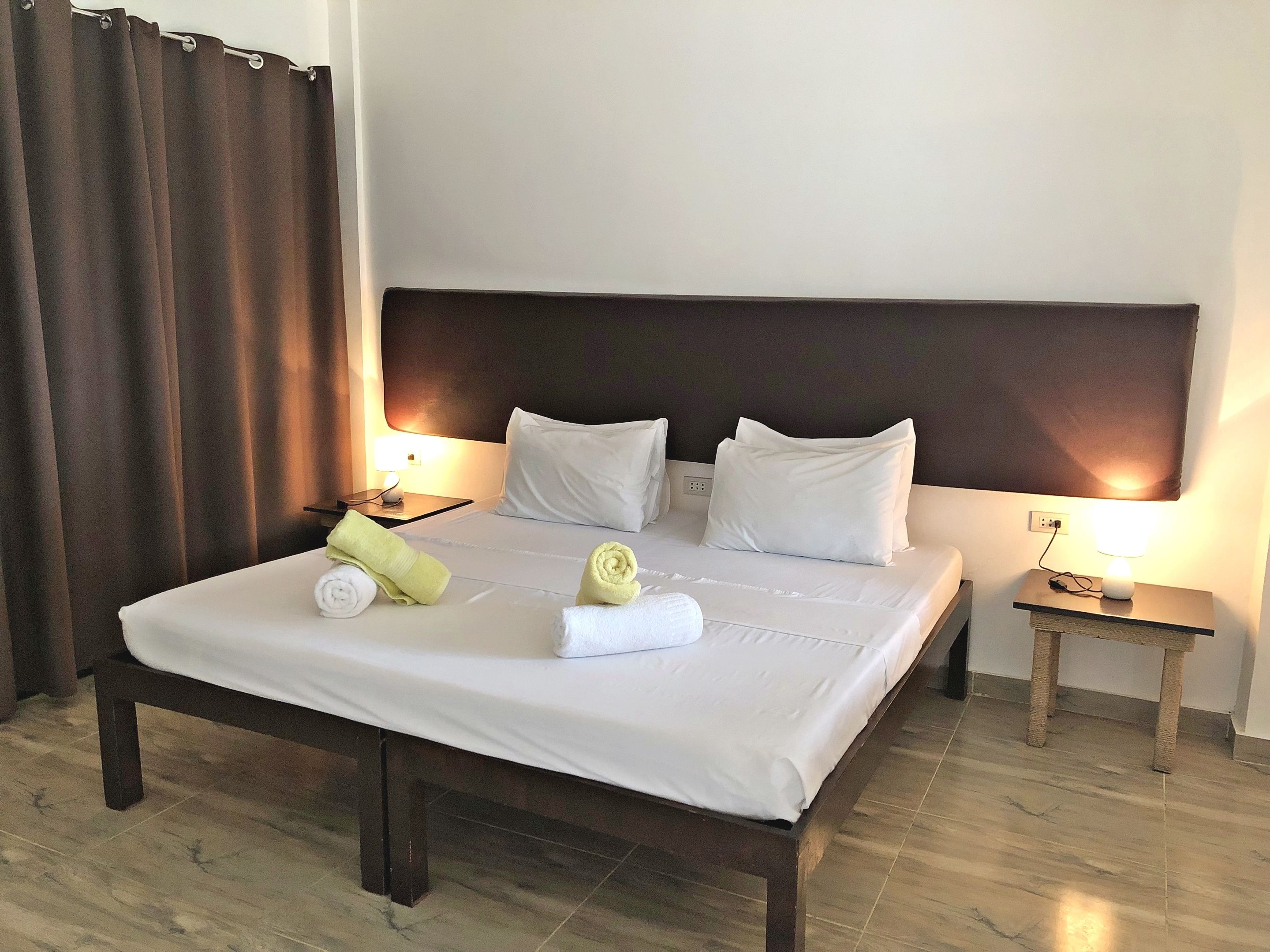 A hotel room with a large bed, two bedside tables, a headboard, and a curtain.