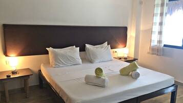 Une chambre d’hôtel avec un grand lit, deux tables de chevet, une petite table et une fenêtre avec des rideaux.