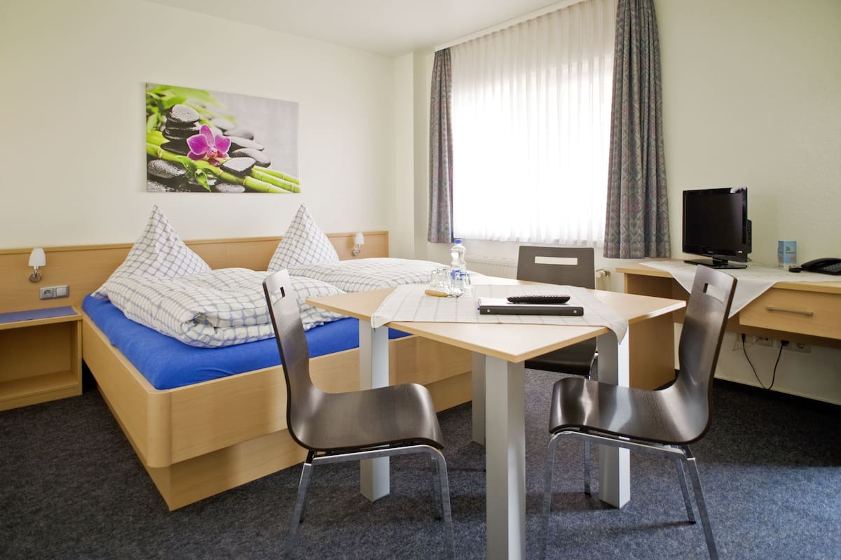 A hotel room with a bed, a desk, two chairs, a TV, and a window with curtains.