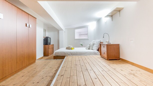 Une chambre avec un plancher en bois, un lit avec des oreillers, une table de chevet, une télévision et une fenêtre.