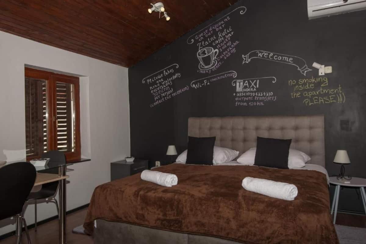 Une chambre d’hôtel avec un lit, un bureau et une chaise. Un mur de la chambre est recouvert d’un tableau noir sur lequel sont énumérés les équipements disponibles.