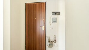 Μια ξύλινη πόρτα με χρυσή χερούλα, ένα θυροτηλέφωνο τοποθετημένο στον τοίχο και ένας διανομέας νερού.