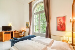 A hotel room with a bed, a desk with a computer, a television, and a window with curtains. - Grandhotel Esplanade (Bad Nenndorf)