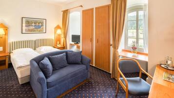Habitación de hotel con cama, sofá, escritorio, silla, televisión y ventana con cortinas.