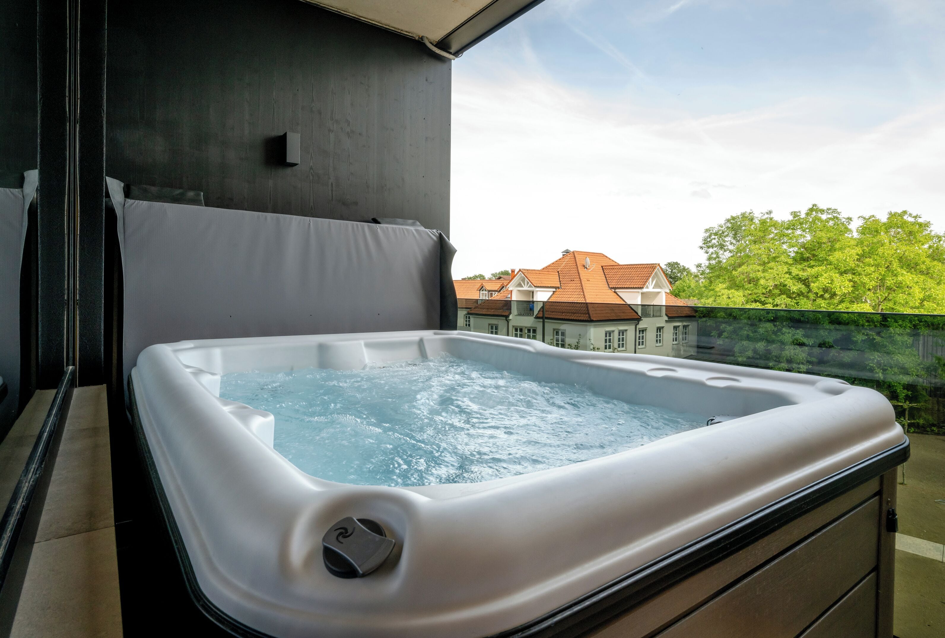 Un jacuzzi en un balcón con vistas a casas y árboles.