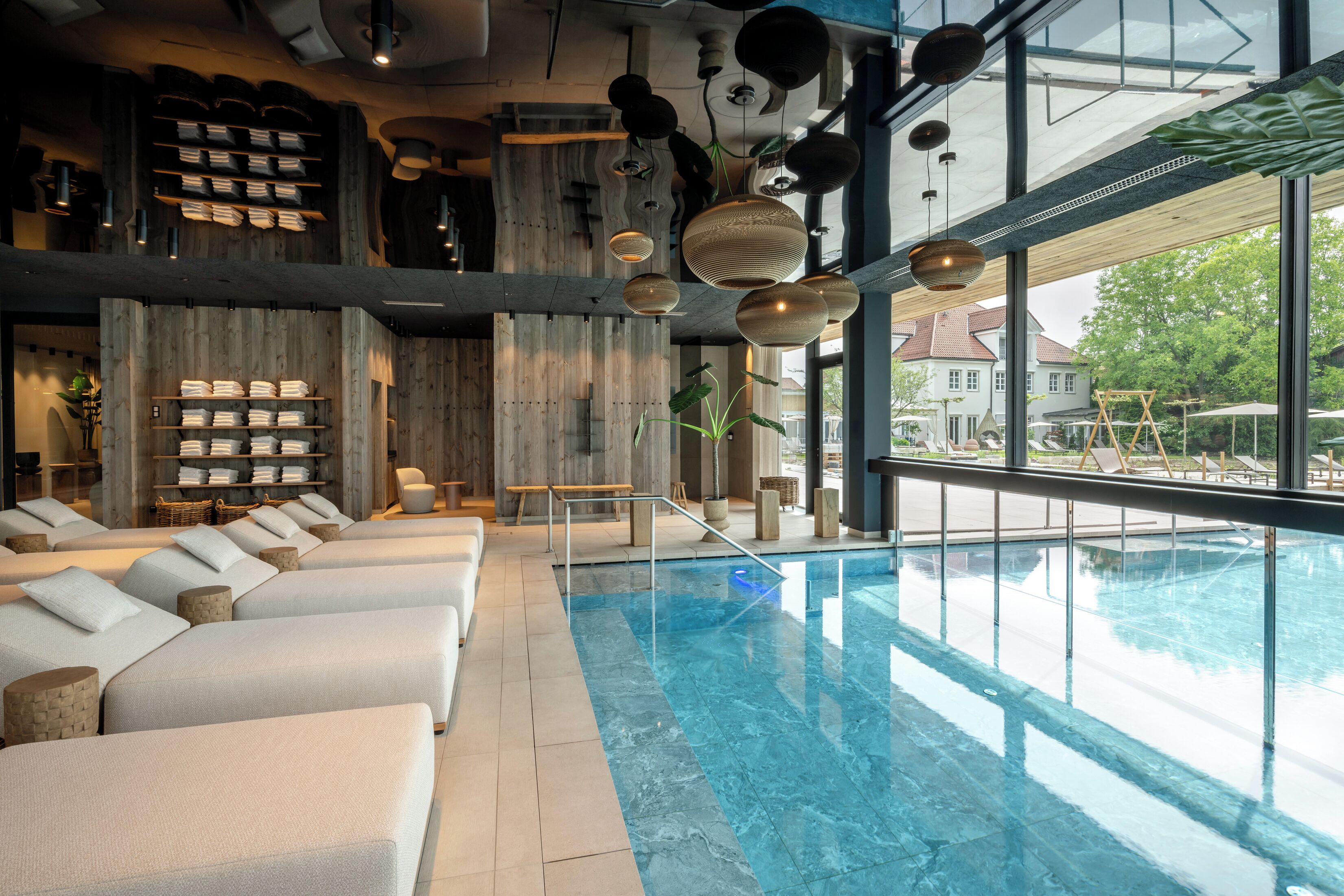 A modern indoor pool area with lounge chairs, a wooden wall, and hanging lights.