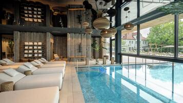 A modern indoor pool area with lounge chairs, a wooden wall, and hanging lights.