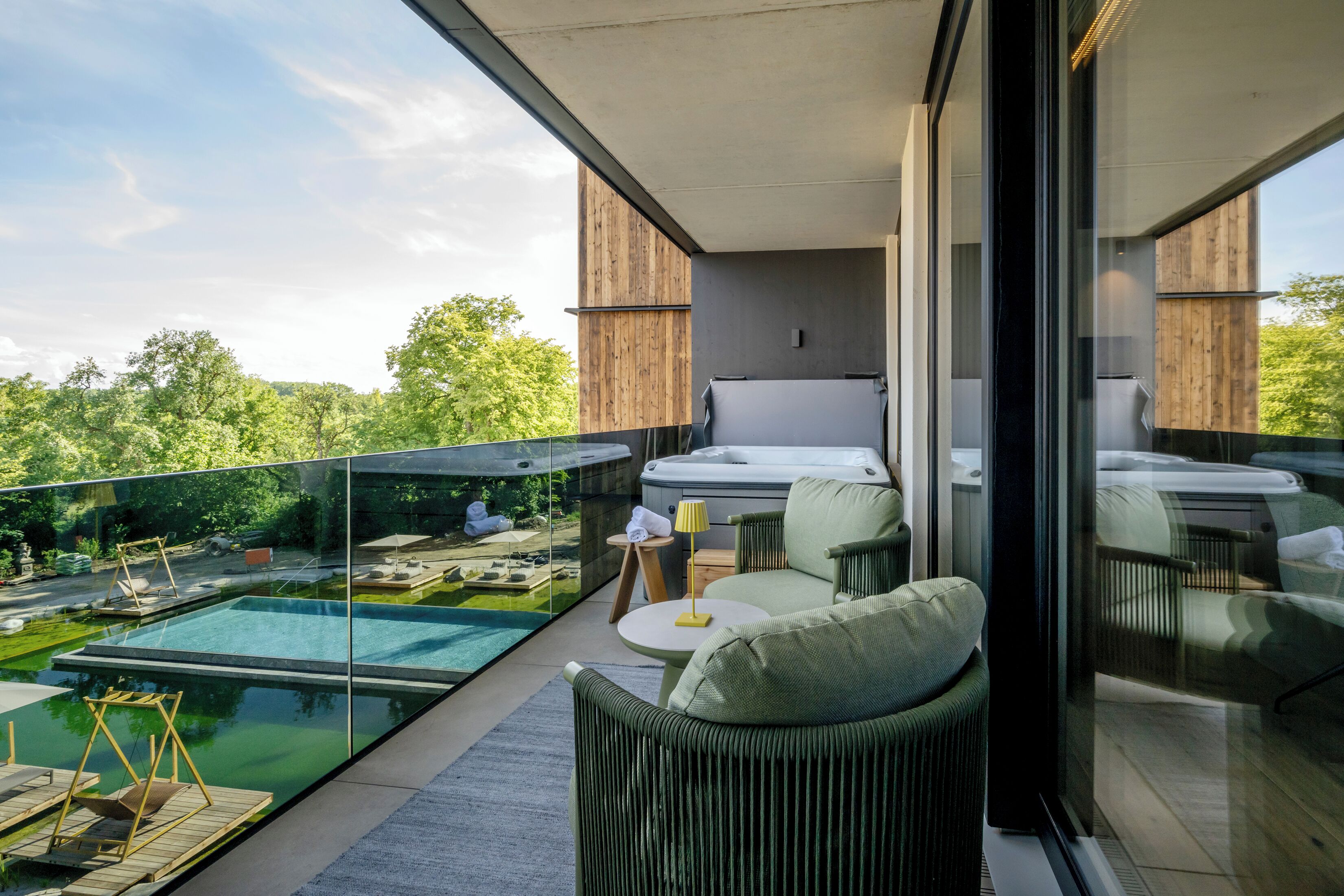 A modern balcony with a glass enclosure, a pool, and outdoor furniture.