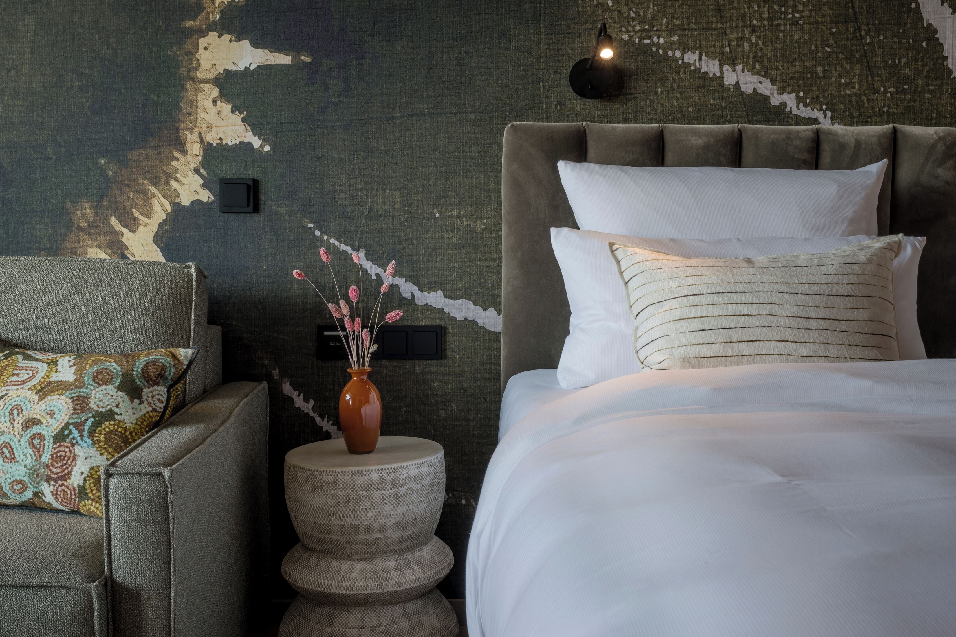 Un dormitorio con una cama grande, una mesita de noche con un florero y una pared con diseño texturizado.