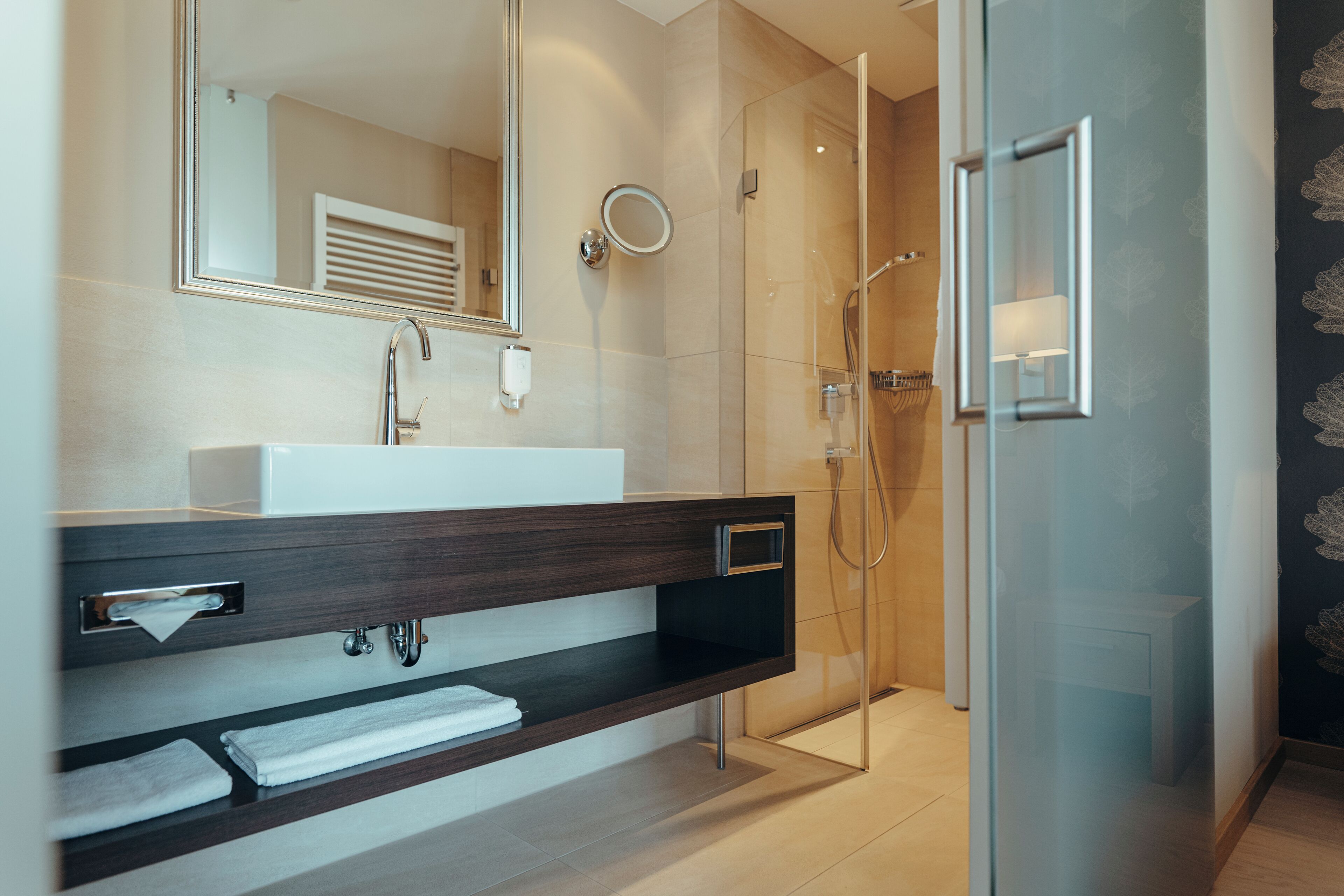 A modern bathroom with a glass-enclosed shower, a large mirror, and a built-in vanity with a towel rack.