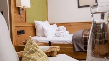 Habitación de hotel con cabecera de madera, cama con sábanas blancas, mesita de noche con lámpara, un cuadro en la pared y un vaso de agua sobre la mesa.