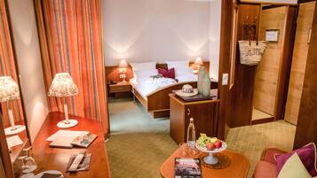 A hotel room with a bed, bedside tables with lamps, a small seating area with a table, and a basket on the wall.