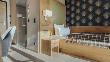 Habitación de hotel moderna con cabecera de madera, cama con manta escocesa, mesita de noche con lámpara y zona de ducha.