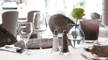 Une table à manger dressée avec des verres à vin, des salières et des poivrières, un vase avec une fleur et une carafe d’eau.