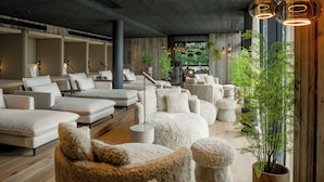 Un área de spa moderna con diversas opciones de asiento, incluyendo sofás y otomanas, dispuestas alrededor de una columna central.