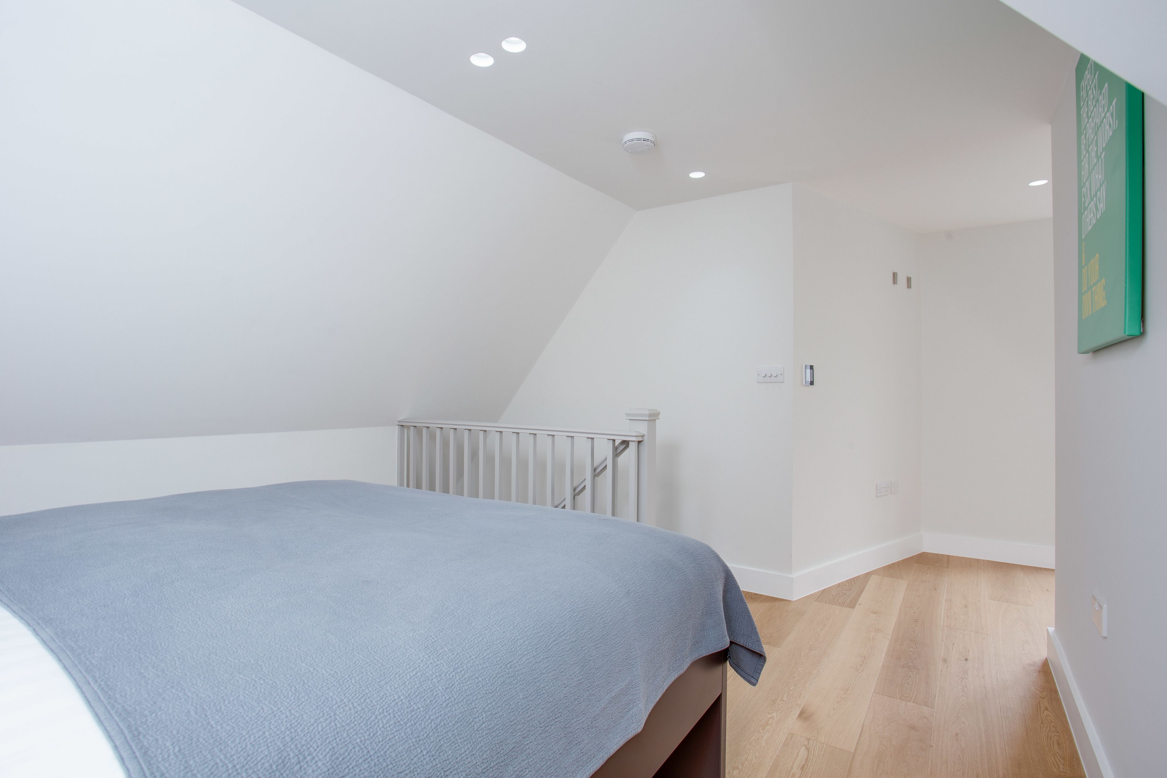 A bedroom with a bed, white walls, a radiator, and a green framed picture on the wall.