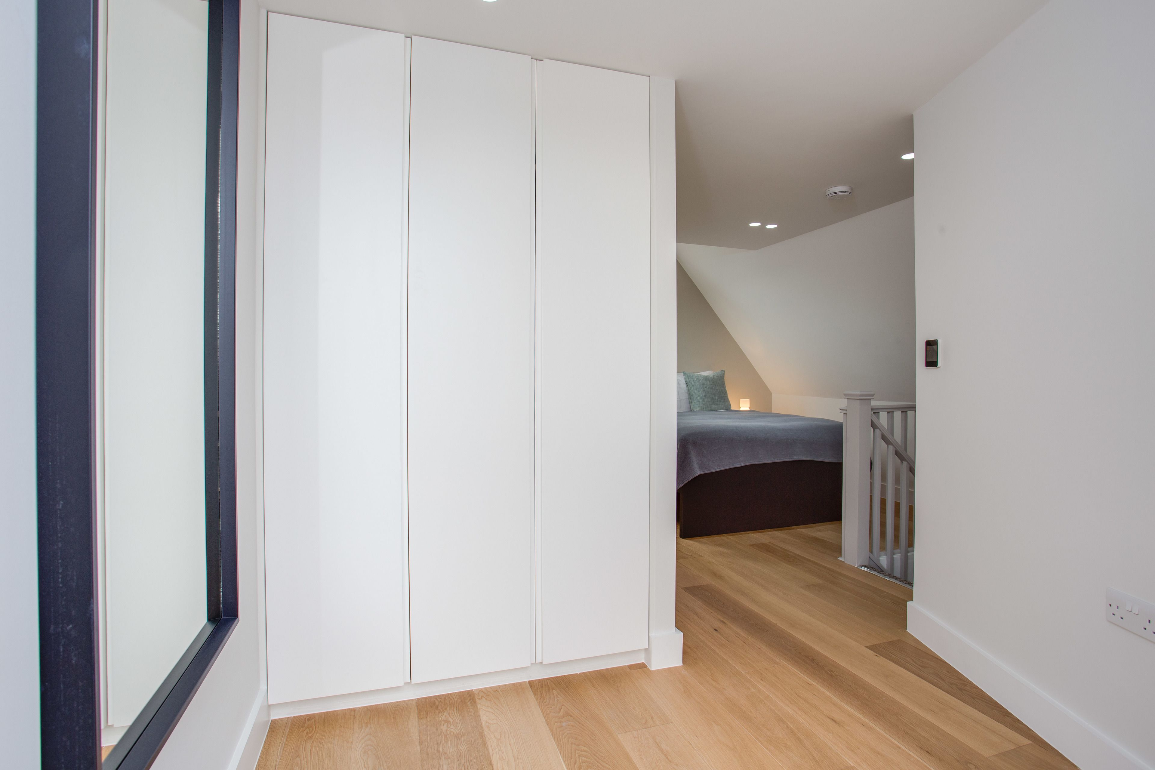 Un couloir avec une armoire blanche, un escalier menant à une chambre, et un plancher en bois.