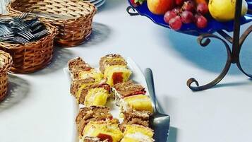 Uma mesa com fatias de bolo, uma fruteira e pratos empilhados.