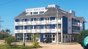 Un hotel llamado HOTEL MURALHA con una estructura de varios pisos, balcones y un coche estacionado frente a él.