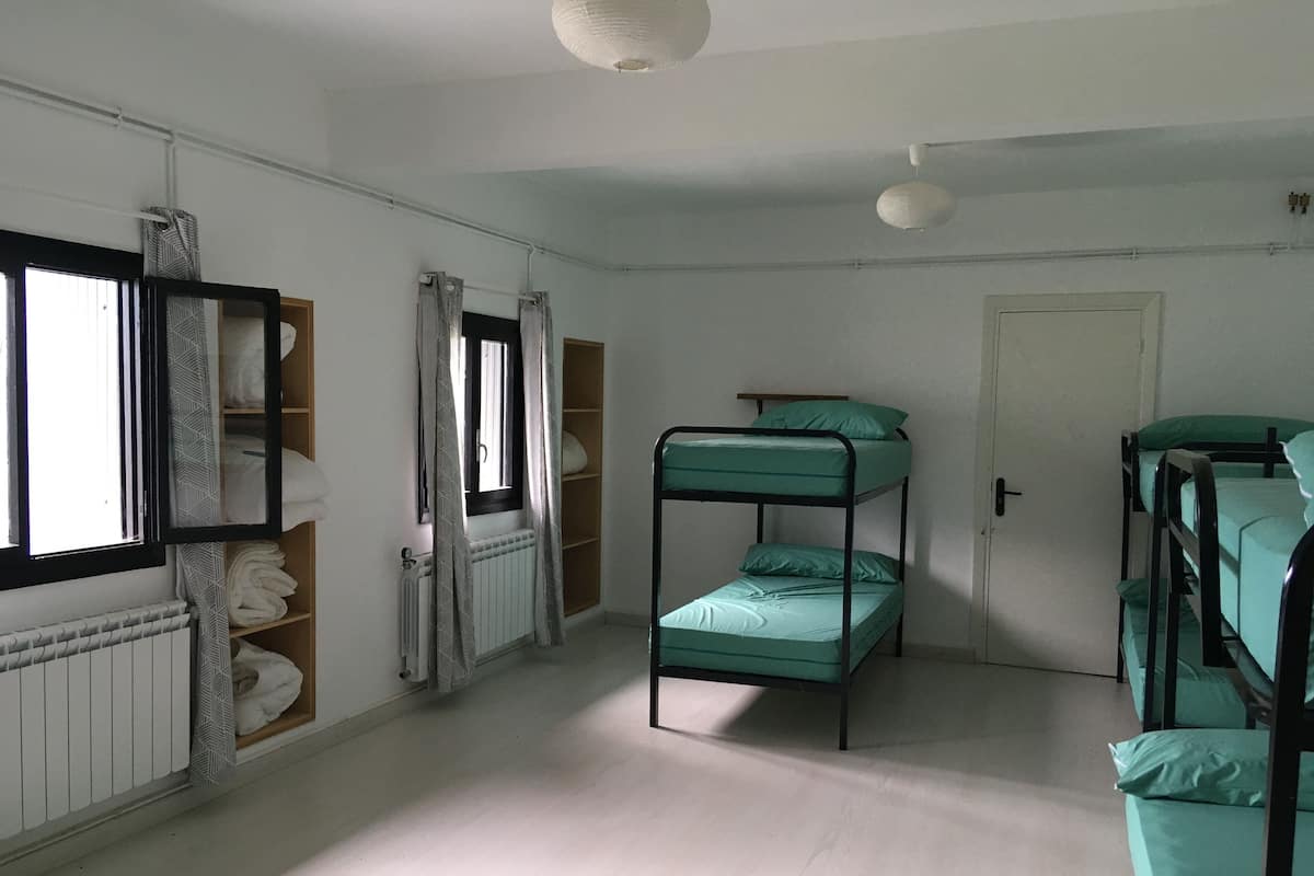 A dormitory room with bunk beds, a radiator, a window with curtains, and a door.