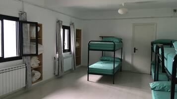 A dormitory room with bunk beds, a radiator, a window with curtains, and a door.