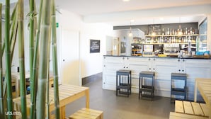 A bar area with wooden stools, a counter with various bottles, and a chalkboard menu. - Albergue Abaraxka - Hostel (Azkoitia)