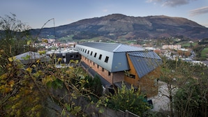 A modern building with a sloped roof, surrounded by greenery and a mountainous backdrop. - Albergue Abaraxka - Hostel (Azkoitia)